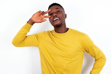 young handsome man wearing yellow sweater over white background making v-sign near eyes. Leisure, coquettish, celebration, and flirt concept.