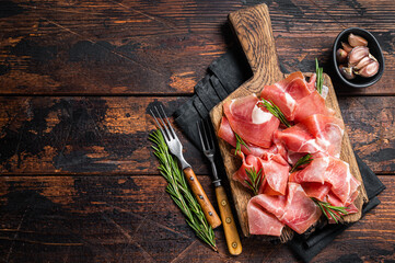 Slices of jamon serrano ham or prosciutto crudo parma on wooden board with rosemary. Wooden background. Top view. Copy space - obrazy, fototapety, plakaty