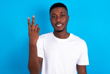 young handsome man wearing white T-shirt over blue background smiling and looking friendly, showing number two or second with hand forward, counting down