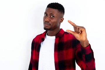 Displeased young handsome man wearing plaid red overshirt over white background shapes little hand sign demonstrates something not very big. Body language concept.