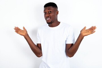 Careless attractive young handsome man wearing white T-shirt over white background shrugging shoulders, oops.