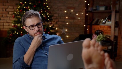 Woman working from home in comfort. Using laptop computer in dark decorated room at home at Christmas in December, Winter.