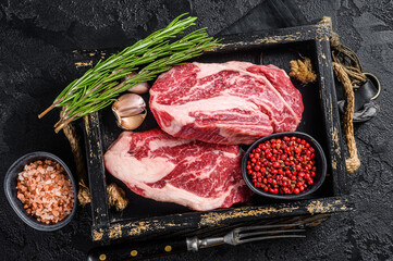 Fresh Raw Chuck roll, Tenders beef steaks in a wooden tray with herbs. Black background. Top view