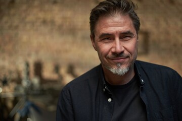 Portrait of mature age, middle age, mid adult casual man in 50s, confident happy smiling. Dark cosy room at home.