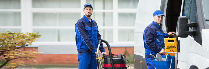 Two Male Janitor Unloading Cleaning Equipment From Vehicle
