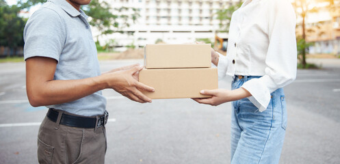 A man in a gray shirt delivers to a woman in a white shirt. The customer receives the mailbox from the delivery person in front of the condo. Freight, online shopping. and logistics concepts