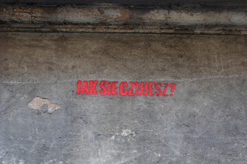 Red inscription on the gray wall of the house in Polish: How do you feel?