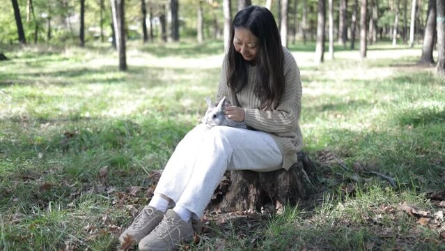 A young smiling woman holds a rabbit. Asian woman wear warm sweater with pet in relax and calm.