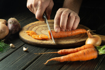 The chef cuts fresh carots on a wooden cutting board. Close-up of cook hands while preparing...