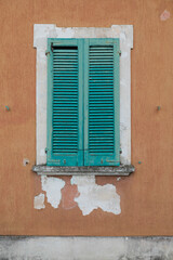 Window with brown wooden shutters on the grey stone brick wall, white frame around the window, vertical format