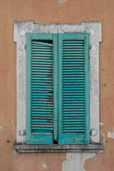 Fototapeta na wymiar Window with closed green damaged wooden shutters, orange and grey house wall with rough surface, no person, vertical format