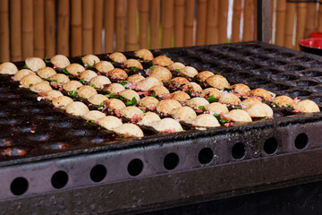 Japanese street food takoyaki at special grill pan. Process of cooking takoyaki balls with octopus...