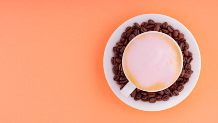 Cup of coffee with pink foam on a coral background. Coffee cup and roasted coffee beans on a saucer. Top view. Copy space