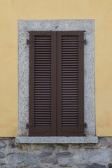 Fototapeta na wymiar Window with brown wooden shutters on a yellow and grey stone brick wall, grey marble frame around the window, vertical format