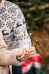 Hands of a man and a woman close-up with a burning sparkler. Festive lights