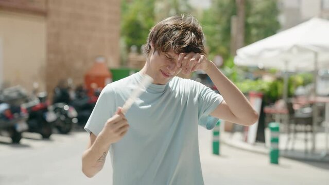 Young blond man using handfan suffering for hot at street