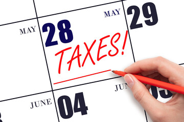 Hand drawing red line and writing the text Taxes on calendar date May 28. Remind date of tax payment