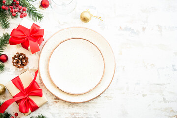 Christmas table setting with craft plate, gift boxes and christmas decorations on light background. Flat lay image with copy space.