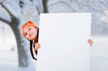 Smiling little young girl child in winter clothes jacket coat and hat holding a blank billboard banner white board