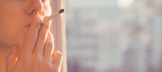 Young man is smoking cigarette near the window.
