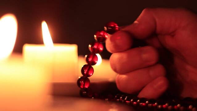 Hand holding rosary against the background of candles