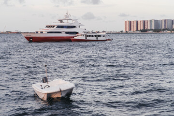 A seascape with several vessels on it: a luxurious safari yacht with a red hull and a smaller doney boat moored to it in the background; a small motorboat tied with a rope in a defocused foreground