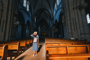 A girl tourist and traveler in a hat explores the majestic interior of a Gothic cathedral or church