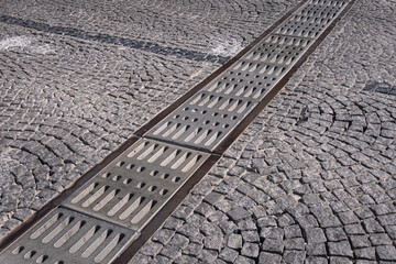 cast iron rainwater drainage grate on cobblestone road