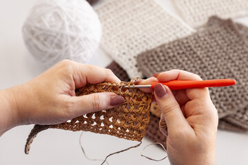 Top view of woman's hands crocheting granny bag with skeins of yarn and finished squares on the background. Craft work concept.