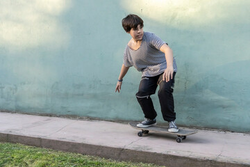 Happy Latin boy is balancing on a skateboard outside the house. Copy space.