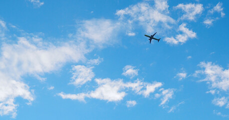 The passenger airplane is flying far away in the blue sky and white clouds. Aircraft in the air. International passenger air transportation. Horizontal stories - obrazy, fototapety, plakaty