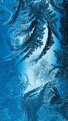 Abstract Christmas vertical background. Blue tinted phone wallpaper. Ice crystals on frozen window glass. Frost drawing. Winter season patterns. Frostwork and frosting pattern. Cold and crystal. Macro