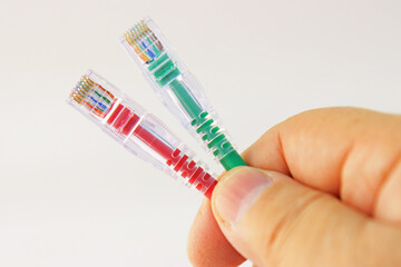 A hand holds a wire with RJ45 connectors on a white background close-up.