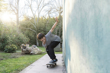 Happy Latin boy is smiling and learning to balance on a skateboard outside the house in a sunny day. Copy space.
