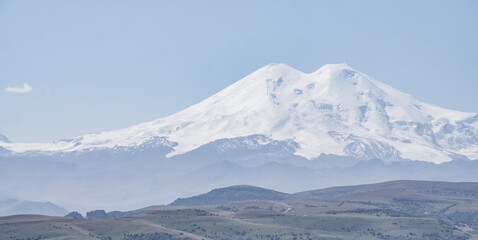 Fototapeta na wymiar Mount Elbrus stands out with two peaks with snow and glaciers panoramic with a clear sky, a warm autumn day