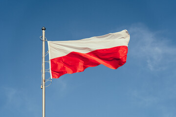 Polska flaga biało-czerwona powiewająca na maszcie na tle błękitnego nieba - obrazy, fototapety, plakaty