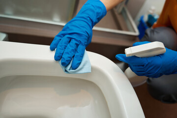 Woman from cleaning company in protective gloves cleaning bathroom fixtures