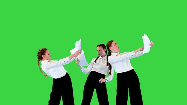 Young caucasian ladies in stage costumes pantomime with sheets of paper, then throw them away and start dancing on a Green Screen, Chroma Key.