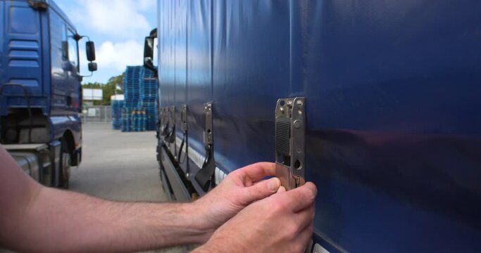Truck driver secures ratchet strap on transport haulage trailer cover