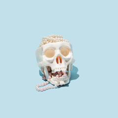 Human skull model, pearl beads in it as a brain, creative horror inspired layout against pastel...