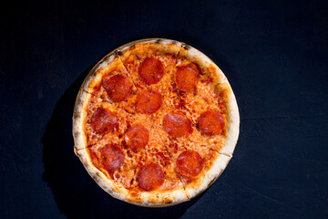 Pizza with tomato sauce, mozzarella, salami on black background. View from above, copy space