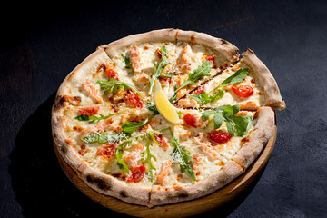 Pizza with salmon, mozzarella, cherry tomatoes, arugula, lemon and parmesan. Italian cuisine