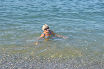 Elderly woman is sitting in the water of beach shallow.