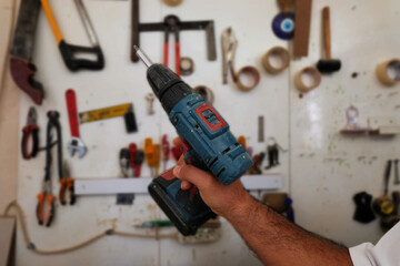 A carpenter holding a cordless screwdriver. Carpenter equipment in the background. carpenter's workshop Close up