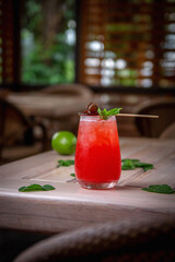 Alcoholic refreshing gin tonic cocktail with strawberry juice, lollipop and mint with ice cubes, on the summer terrace of the restaurant.