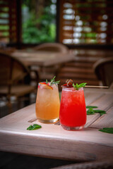 Alcoholic refreshing gin tonic cocktail with strawberry juice, lollipop and mint with ice cubes, on the summer terrace of the restaurant.