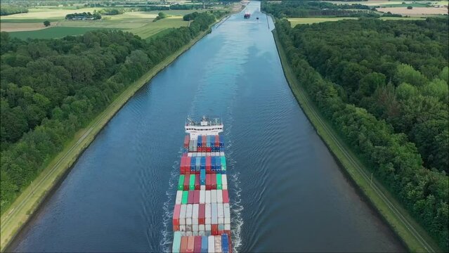 Aerial top down view over the container ship following along Kiel Kanal. The view of container ship from the air. Birdseye view flying low around large cargo ship passing Kiel Kanal.