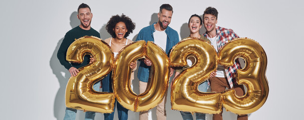 Group of young beautiful people in casual clothing carrying gold colored numbers and smiling