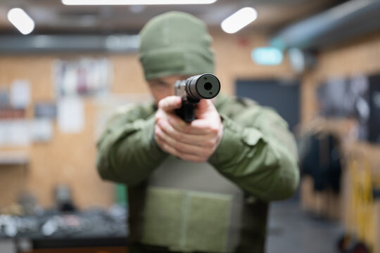 A man is aiming a pistol with a silencer, front view, soft focus photo, the main focus is on the silencer.