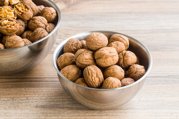 Newly harvested walnuts, designed in stainless steel bowls, on a wooden table,conceptual image